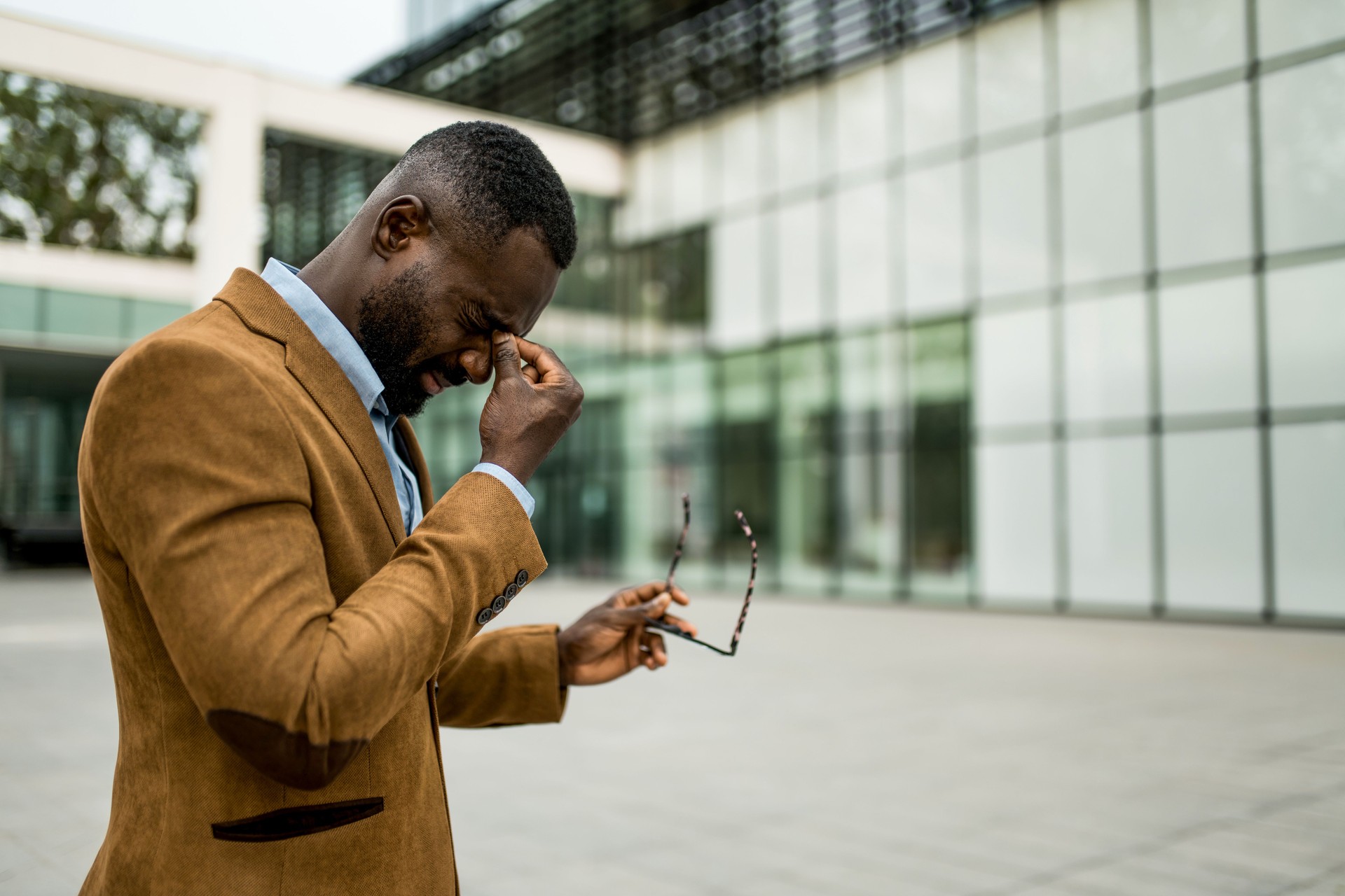 Tired black businessman having eyesight problems outdoors.