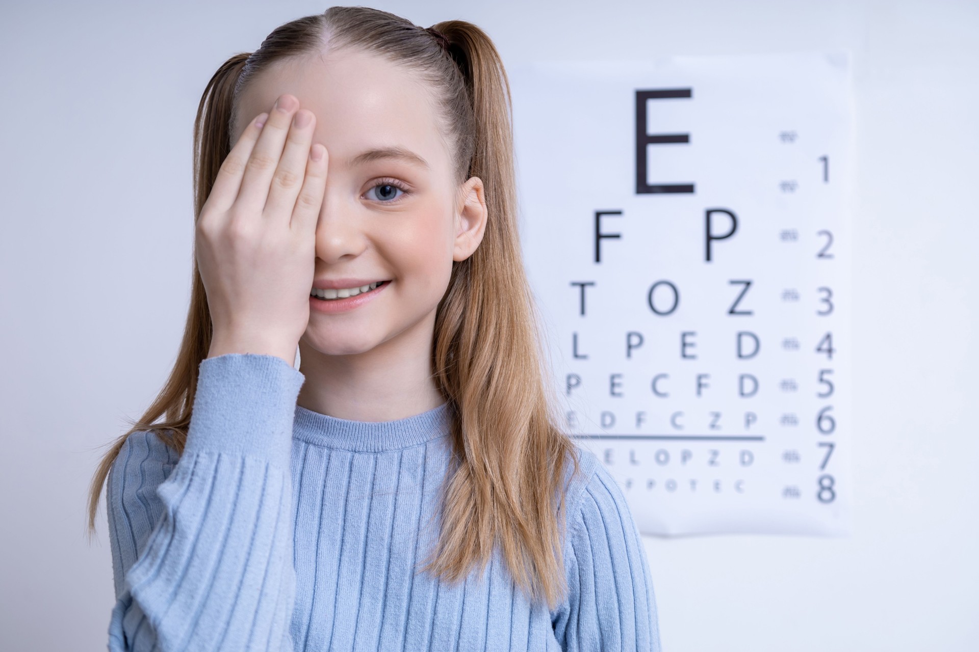 Cute caucasian girl on the Snellen vision test background at the ophthalmologist office