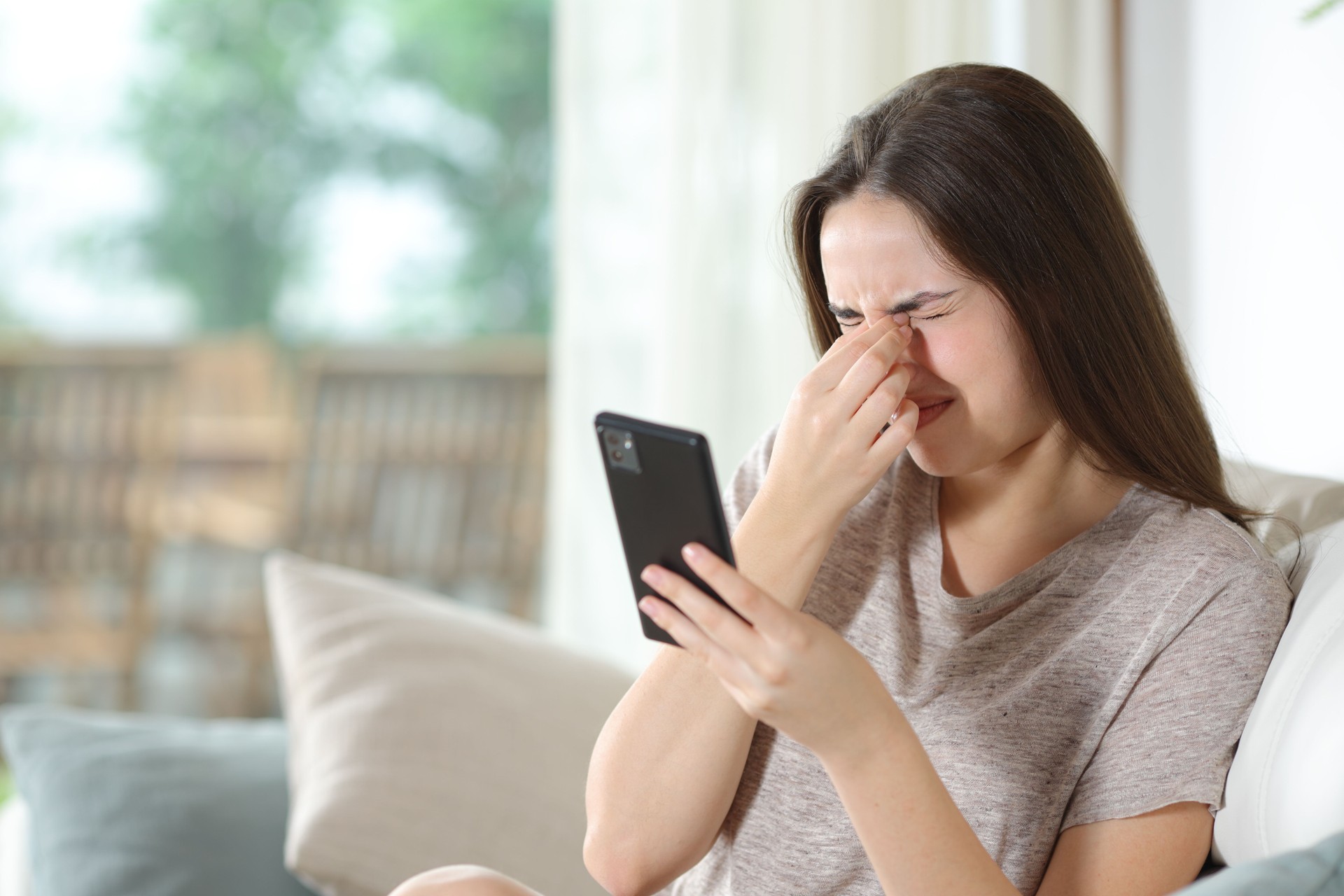 Woman using phone suffering eye strain at home Woman using phone suffering eye strain at home